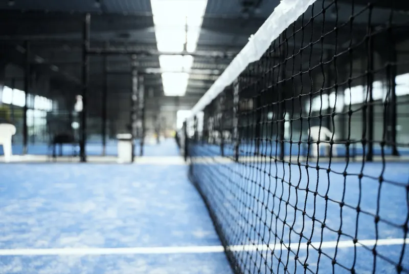 A padel net running down a row of indoor blue courts